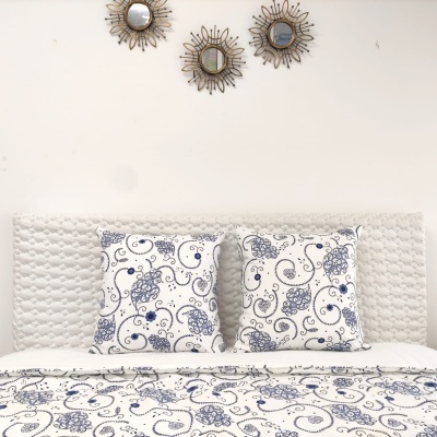 Cama branca com almofadas e manta estampadas em azul e branco, cabeceira estofada e espelhos decorativos na parede