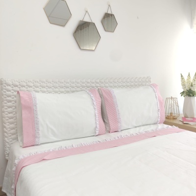 Cama com lençóis brancos e rosa, cabeceira texturizada, espelhos hexagonais e decoração de mesa