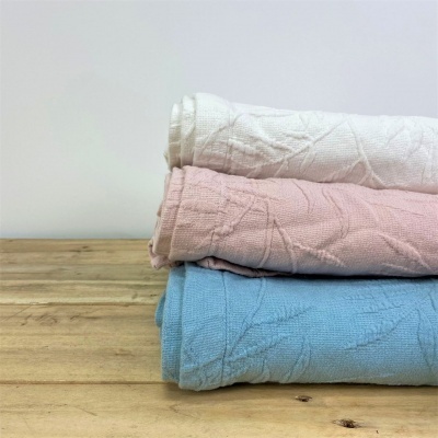 Três mantas empilhadas nas cores branco, rosa claro e azul claro sobre mesa de madeira