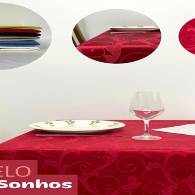 Toalha de mesa vermelha com padrão floral em relevo sobre mesa com prato, taça e castiçal.