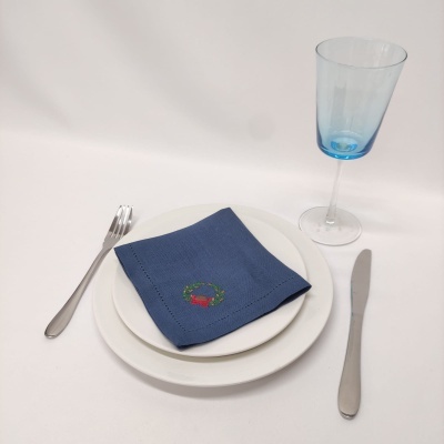 Conjunto de jantar com pratos brancos, guardanapo azul bordado, talheres prateados e taça azul