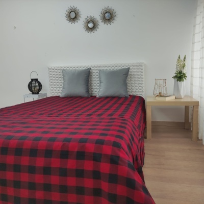 Cama com edredão xadrez vermelho e preto, almofadas cinza e mobiliário claro