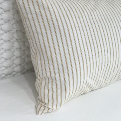 Almofada com riscas verticais bege sobre superfície branca e fundo de estofado texturado branco