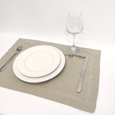 Conjunto de jantar com pratos brancos, talheres, taça e individual bege bordado.