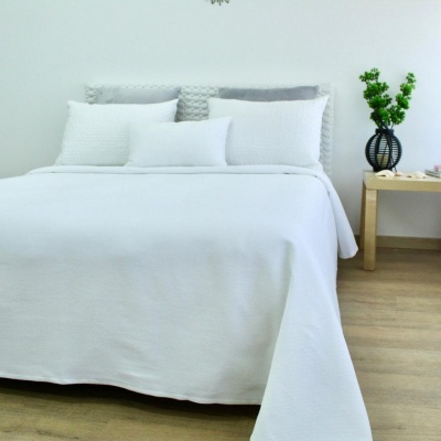 Cama com roupa de cama branca, cabeceira cinzenta e mesa de madeira com vaso e planta