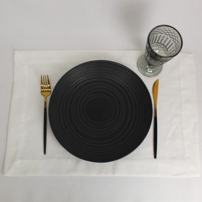 Conjunto de jantar com prato preto, talheres pretos e dourados e copo de vidro sobre base branca