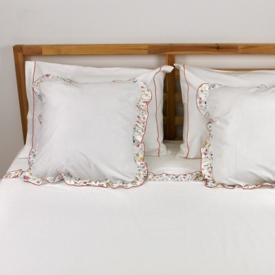 Almofadas brancas com bordado floral colorido e linha vermelha, em cama de madeira clara