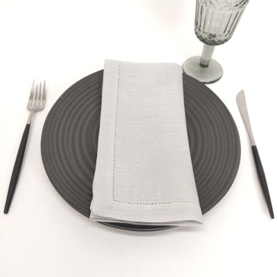 Conjunto de jantar com prato cinza escuro, guardanapo branco, talheres com cabo preto e copo de vidro translúcido