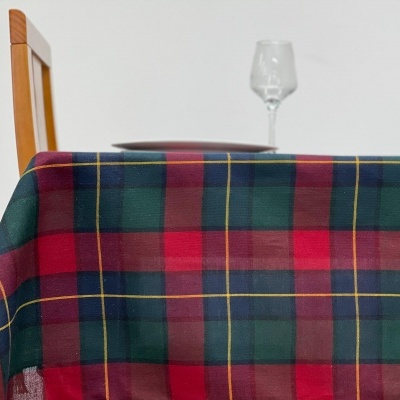 Toalha de mesa xadrez vermelha, verde e azul sobre mesa com cadeira e copo de vidro.