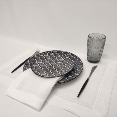 Conjunto de loiça azul com padrão de escamas, talheres pretos, guardanapo branco e copo cinza sobre toalha branca.