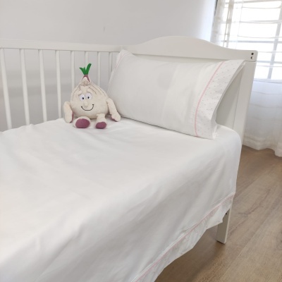Cama de bebé branca com roupa de cama branca e detalhes cor-de-rosa, brinquedo de pelúcia e chão de madeira