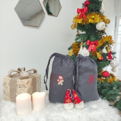 Dois sacos cinzentos com decorações natalícias junto a velas, presente rústico e árvore de Natal decorada