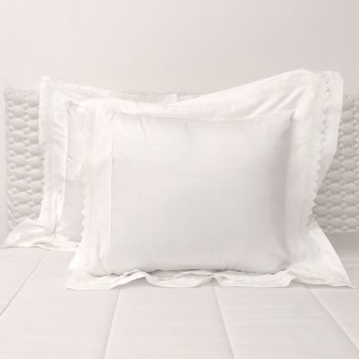 Três almofadas brancas de vários tamanhos e texturas sobre uma cama branca