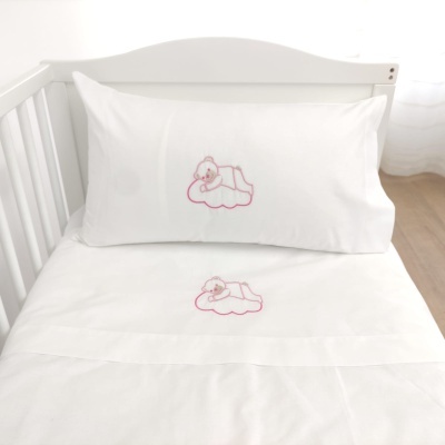 Cama de bebé branca com lençol e fronha bordados com ursinho rosa numa nuvem cor-de-rosa