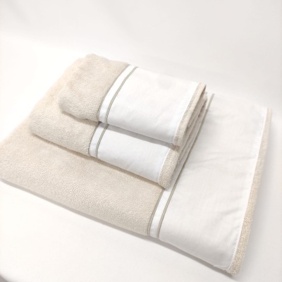 Conjunto de toalhas bege e branca com faixa decorativa, empilhadas