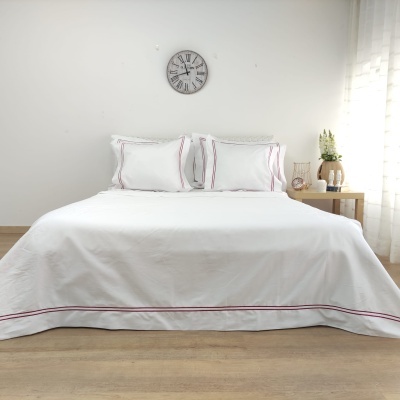 Cama com roupa de cama branca e detalhes vermelhos, relógio e mesa com decoração