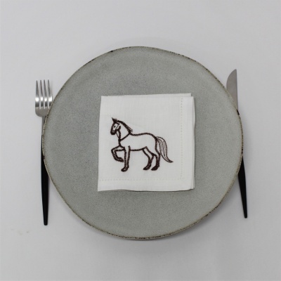 Prato cinza com guardanapo branco bordado com cavalo e talheres pretos.