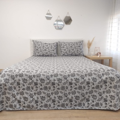 Cama de casal com colcha e almofadas florais cinza e preto, espelhos geométricos na parede e mesa com vaso decorativo