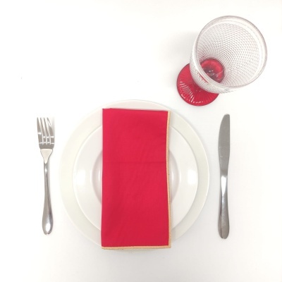 Prato branco com guardanapo vermelho, garfo, faca e copo transparente com base vermelha em fundo branco