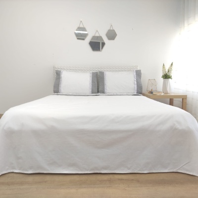Cama de casal com roupa de cama branca e fronhas riscas cinza numa decoração minimalista com espelhos geométricos e mesa de cabeceira