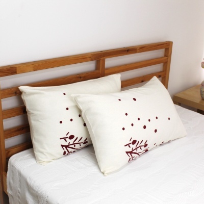 Almofadas brancas com padrão vermelho sobre cama com cabeceira de madeira clara