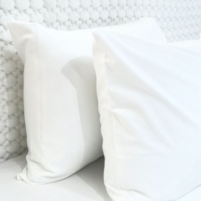 Dois almofadões brancos sobre cama com cabeceira branca estofada