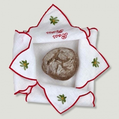 Pão rústico redondo em tecido branco bordado com texto e folhas verdes