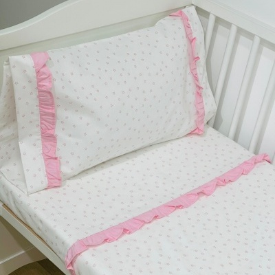 Roupa de cama para bebê branca com motivos e folhos cor-de-rosa em cama branca