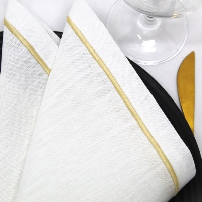 Guardanapo branco com linha dourada em prato preto com faca dourada e copo
