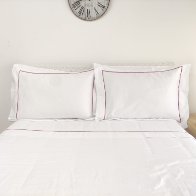 Jogo de cama branco com linhas vermelhas e relógio antigo na parede