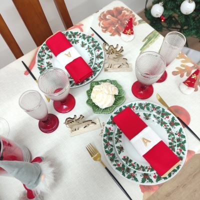 Mesa de Natal decorada com pratos, guardanapos vermelhos, copos com base vermelha e decorações de rena de madeira
