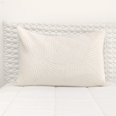 Almofada branca retangular com padrão geométrico em relevo sobre cama branca com cabeceira texturada