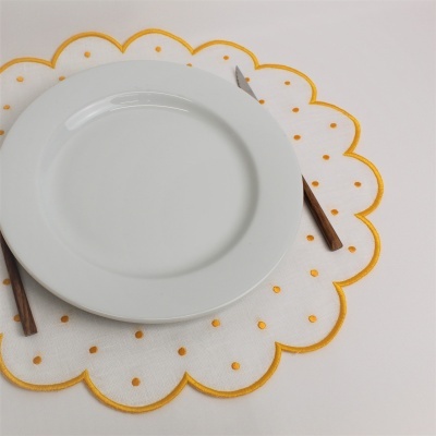 Prato branco redondo em cerâmica sobre um individual branco com pontos amarelos e borda ondulada, com talheres de cabo castanho