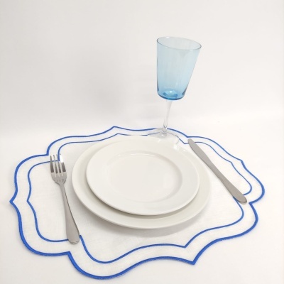 Conjunto de pratos brancos, talheres de metal, copo azul e base branca com contorno azul