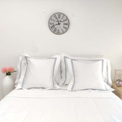 Conjunto de roupa de cama branca com almofadas de bordas azuis e decoração simples