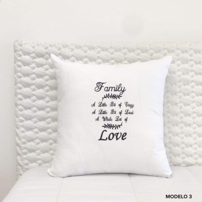 Almofada branca quadrada com texto bordado em preto sobre cama branca