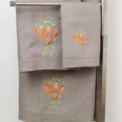 Toalhas cinzentas com bordado floral laranja e verde penduradas num suporte prateado