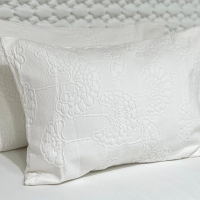 Duas almofadas brancas bordadas sobre cama branca com padrão texturizado