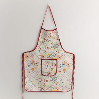 Avental colorido com padrões florais e remate vermelho pendurado numa parede branca