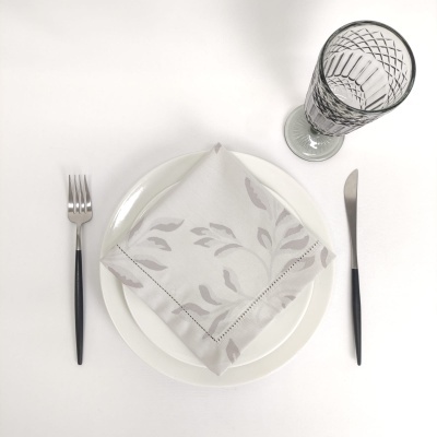 Conjunto para refeição com prato branco, guardanapo cinza, talheres com cabo preto e copo de vidro com padrão geométrico