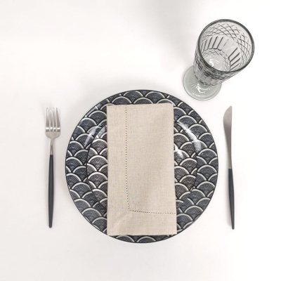 Conjunto de mesa com prato decorado, guardanapo bege, talheres com cabo preto e copo de vidro.