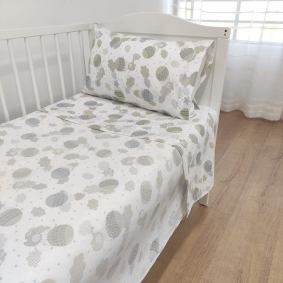 Cama infantil branca com lençol e fronha estampados com ovelhas e bolas em tons pastel