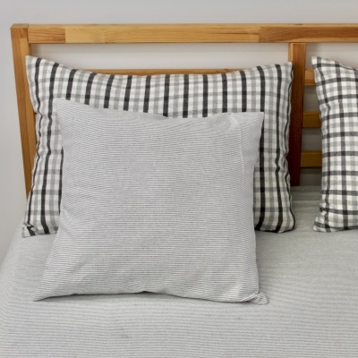 Almofadas em cama, duas com padrão xadrez preto e branco, uma cinzenta com riscas finas.