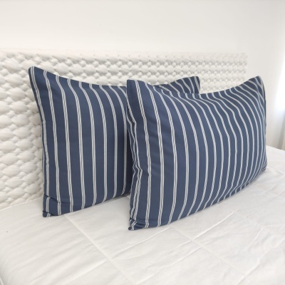 Duas almofadas azul com riscas brancas num colchão branco