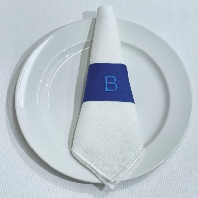 Guardanapo branco com porta-guardanapo azul com letra B sobre prato branco