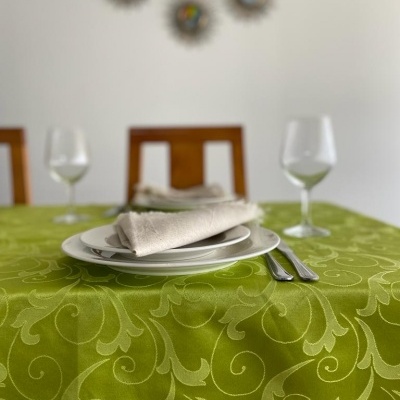 Mesa com toalha verde padronizada, pratos brancos, talheres de metal, copos de vidro e decoração circular na parede