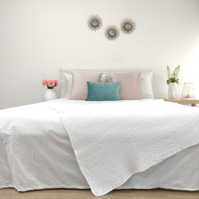 Cama branca com quatro almofadas coloridas, manta branca e três espelhos decorativos na parede