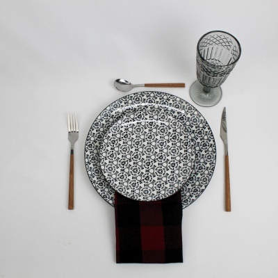 Conjunto de jantar com pratos brancos com padrão preto, talheres com cabo de madeira, guardanapo e copo transparente
