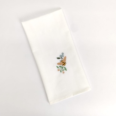 Pano de cozinha branco com bordado de abelha e folhas verdes