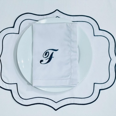 Guardanapo branco com letra 'F' sobre prato branco em toalha branca com padrão preto